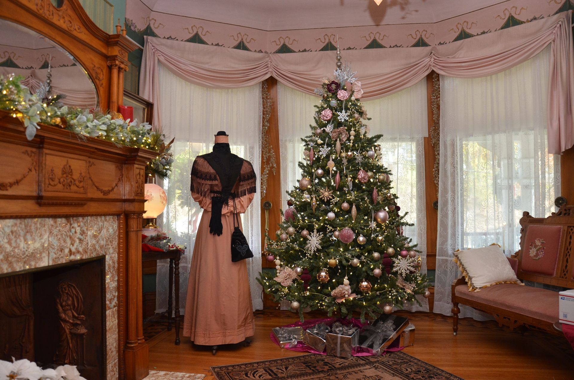 Victorian-style room with a decorated Christmas tree, a mannequin in a dress, and a fireplace.