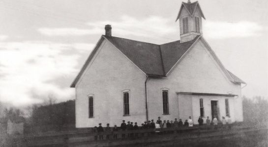 Old white church with steeple; group of people in front.