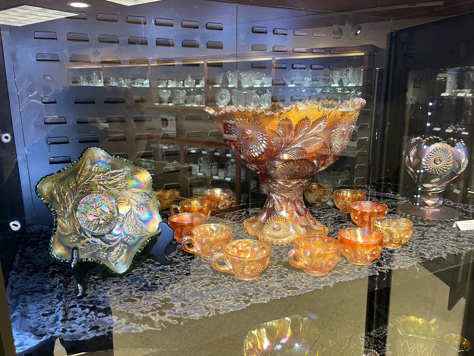 Display of iridescent amber glass bowls and dishes in a cabinet; various shapes and sizes.