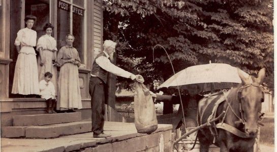 Man with bag by horse-drawn carriage in front of Post Office. Women on porch.