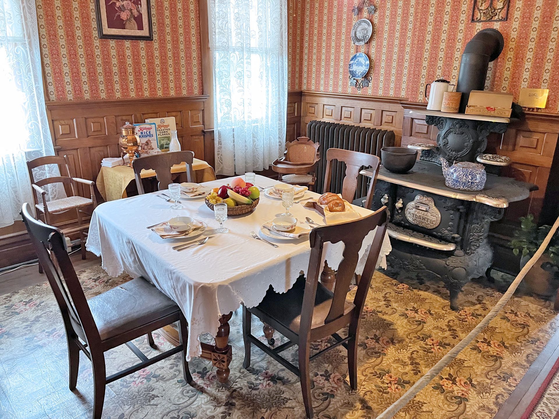 Dining room with a table set for a meal, a vintage stove, and patterned wallpaper.