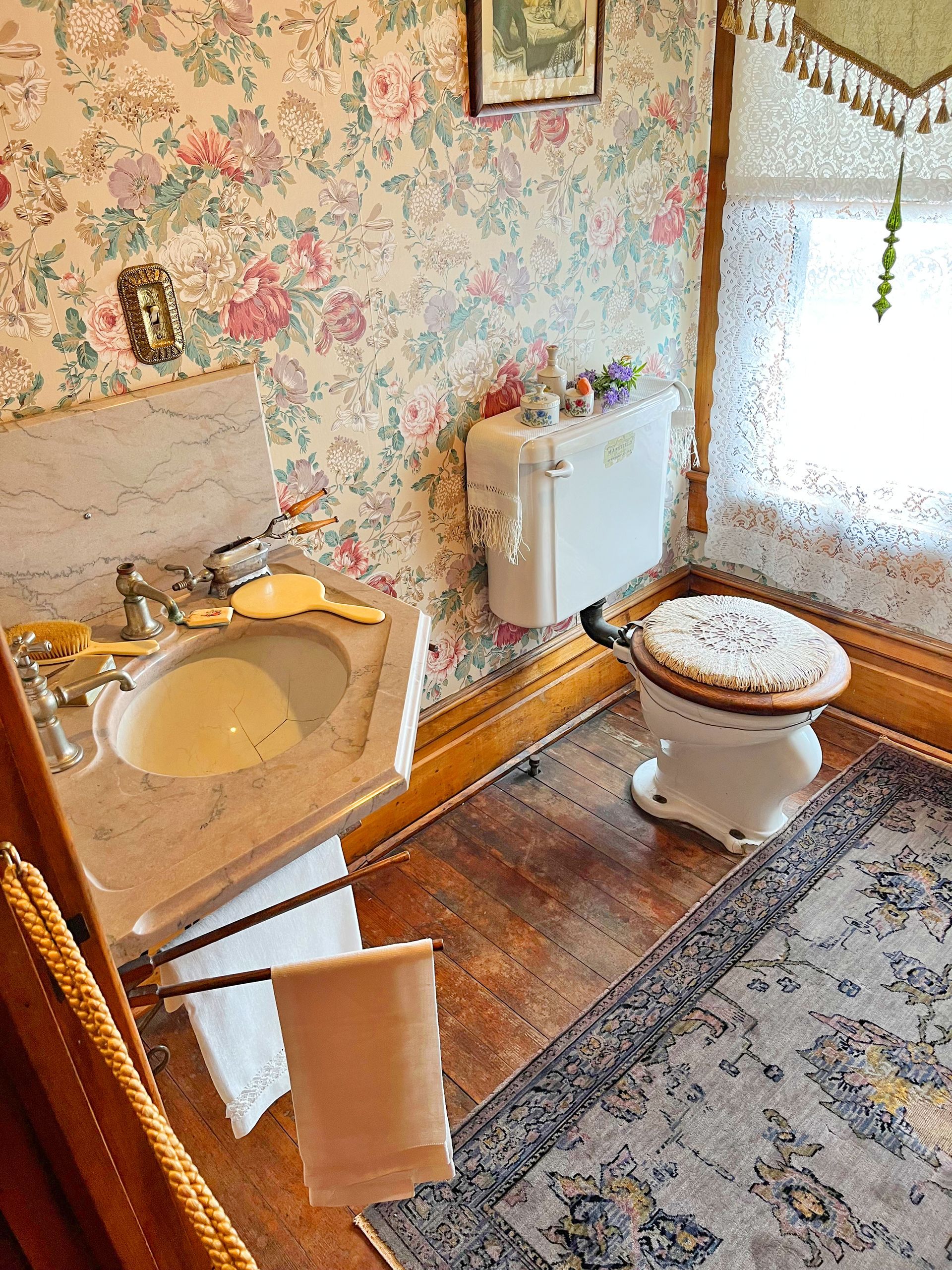 Bathroom with floral wallpaper, marble sink, vintage toilet, and rug.