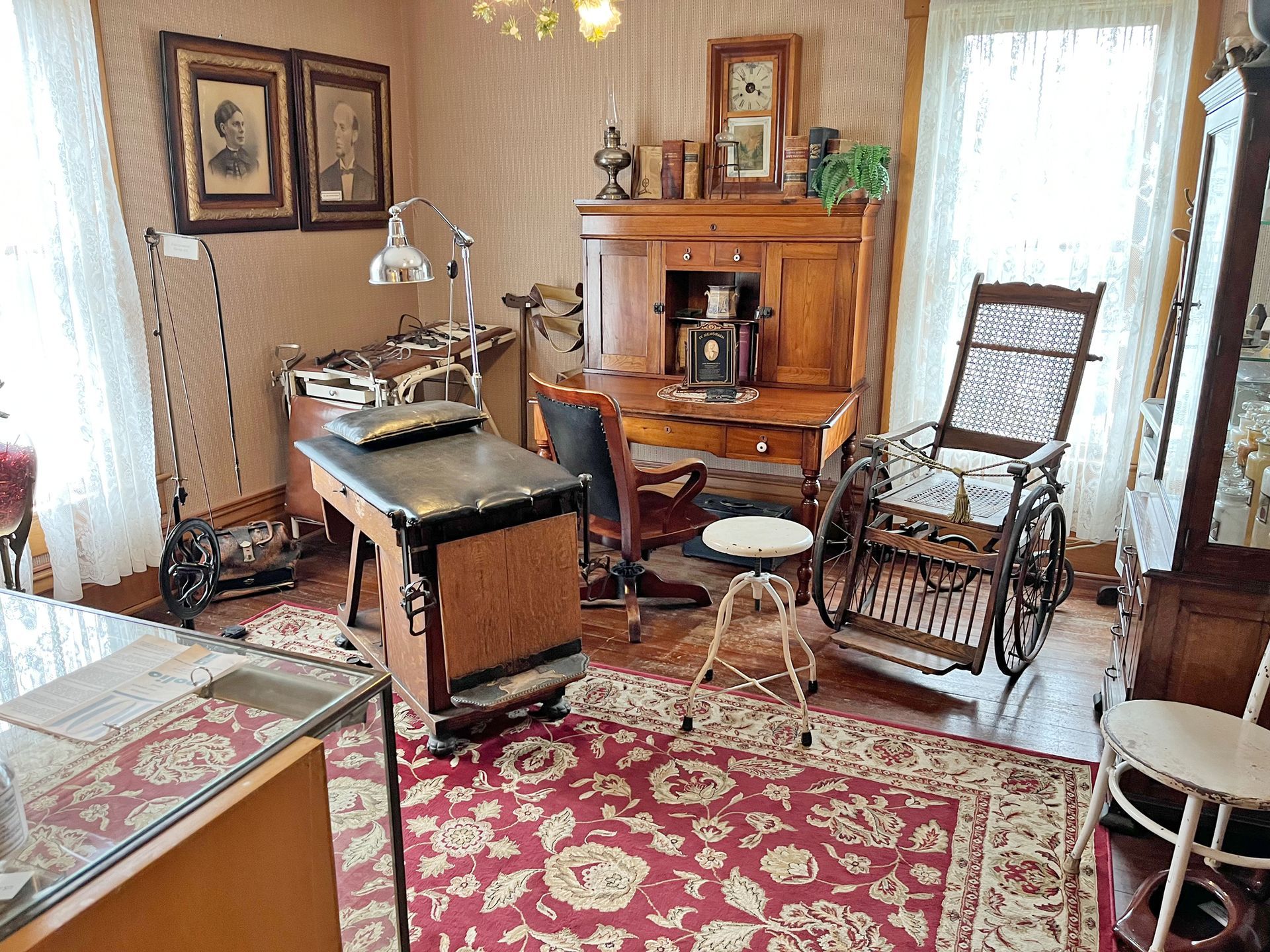 Antique doctor's office with exam table, desk, wheelchair, and medical instruments on display.