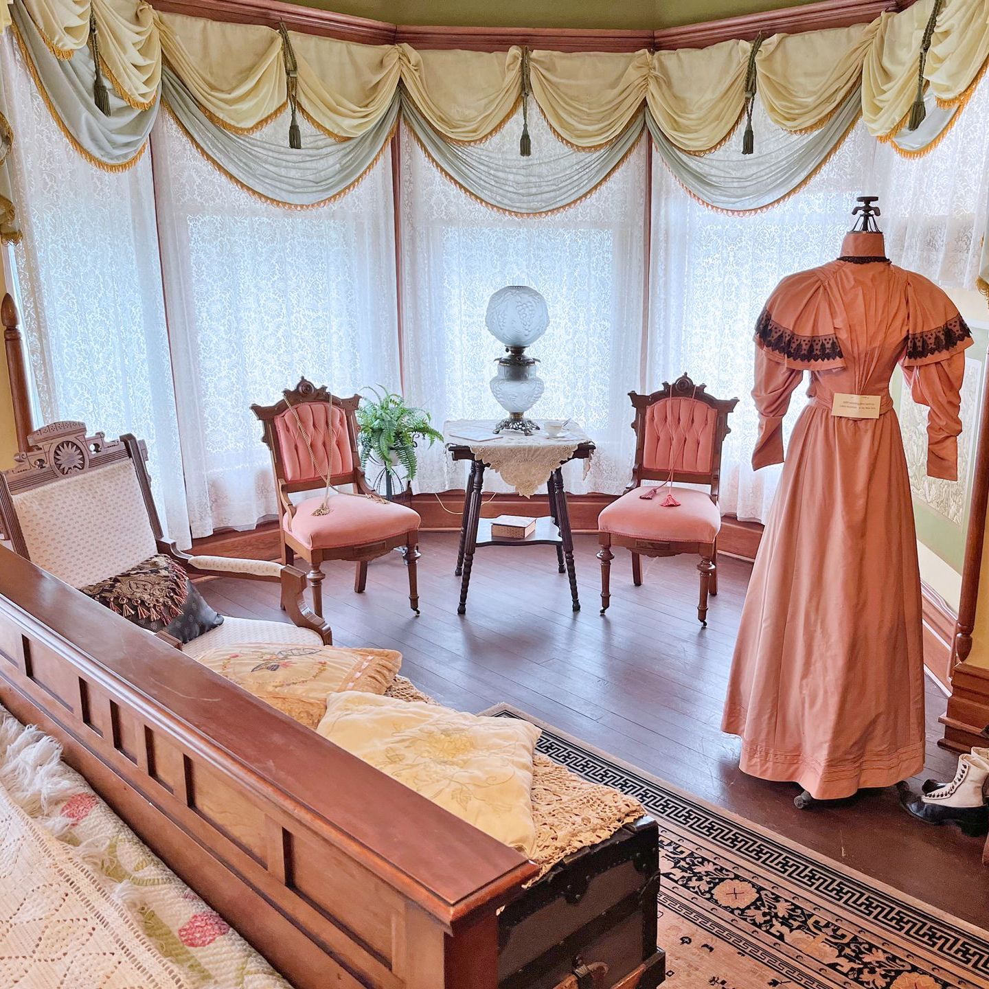 Victorian-era room with a dress form, chairs, and a table in front of a window.