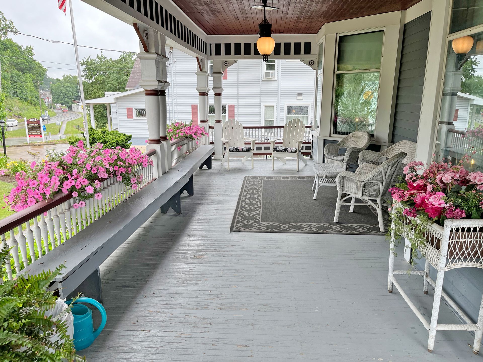Covered porch with white railings, pink flowers, and seating.