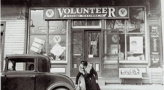 Volunteer Food Stores storefront; person in front, car partially visible. Vintage black and white photo.