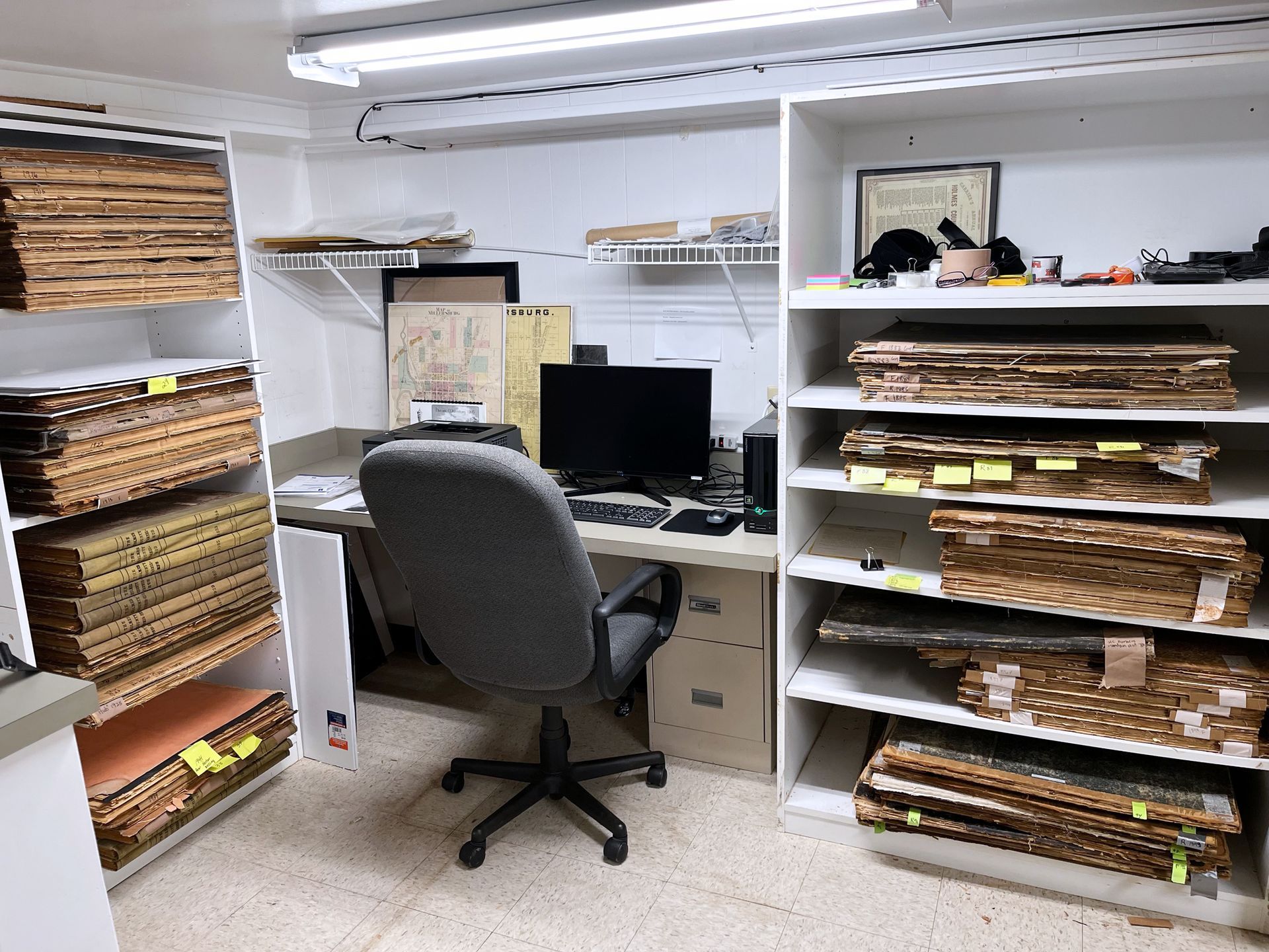 Small office with desk, computer, shelves filled with papers and folders.
