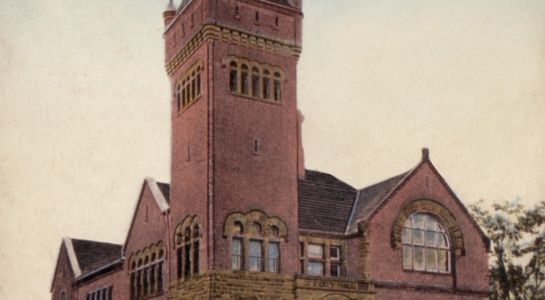 Brick building with tall tower and arched windows, likely historic architecture.