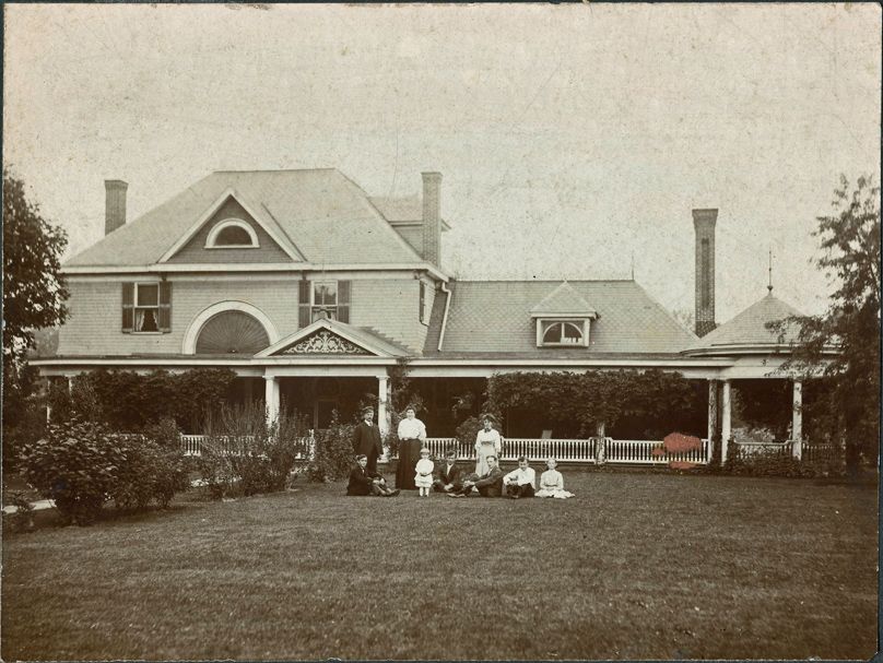 Large house with family in front; garden, porch, gazebo, and lawn.