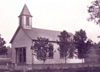 Old, wooden church building with a small steeple, behind a picket fence.