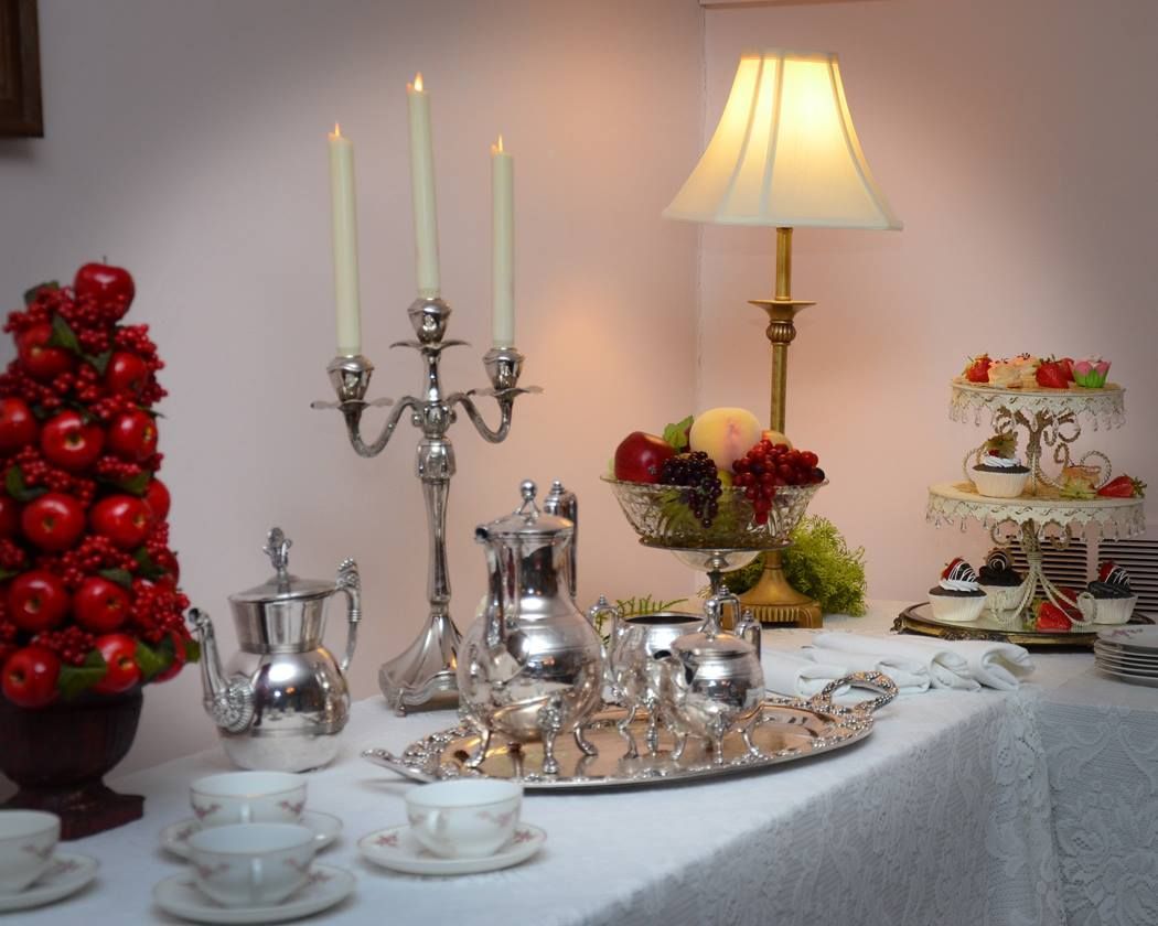 Elegant table setting with silver tea service, candles, fruit, and small cakes.