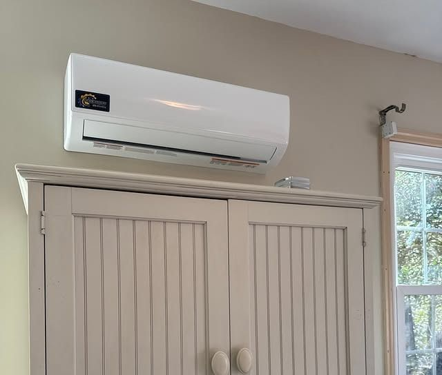 White wall-mounted air conditioner above a white wardrobe near a window in a bright room
