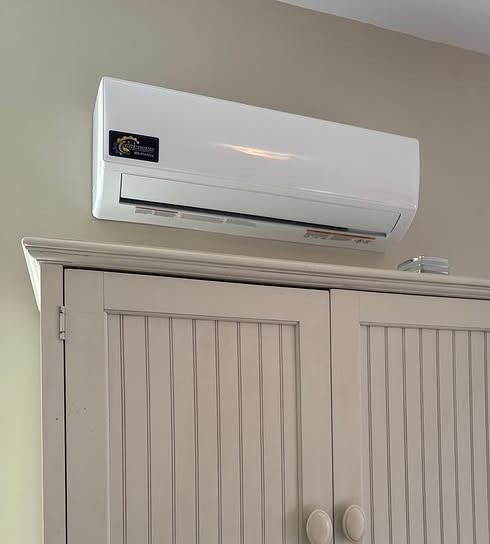 Wall-mounted white air conditioner above a beige closet cabinet indoors