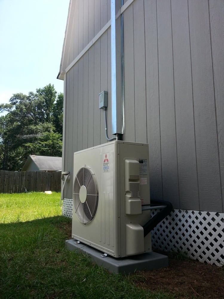 Outdoor HVAC unit mounted on a gray house wall beside a grassy yard.
