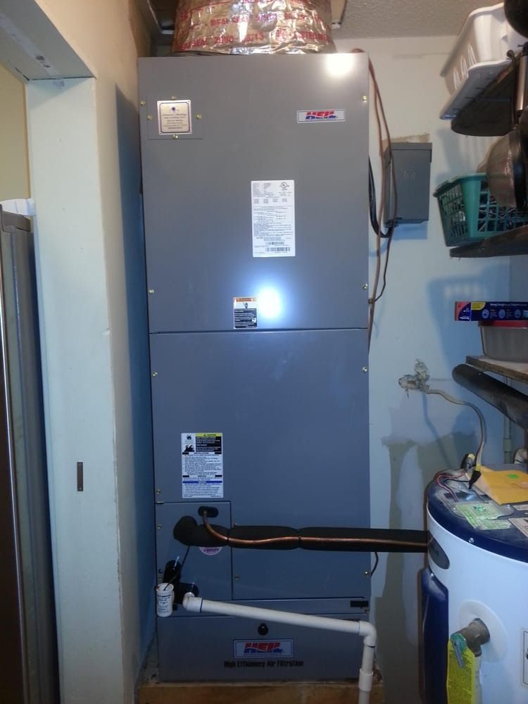 Utility closet with a gray HVAC furnace, white water heater, and pipes in a narrow room