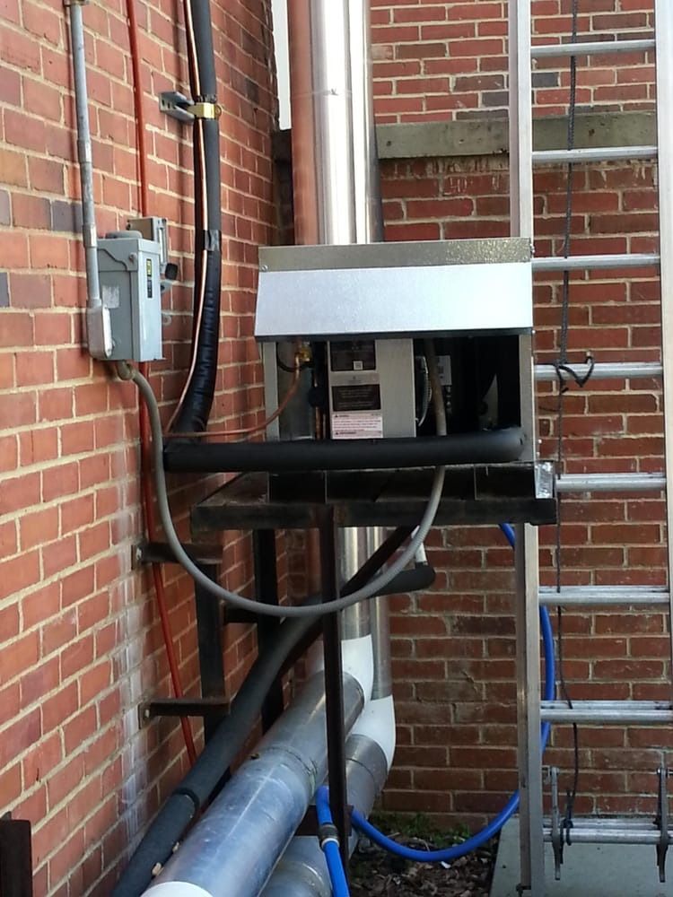Outdoor utility equipment mounted on a brick wall with black hoses and metal pipes.