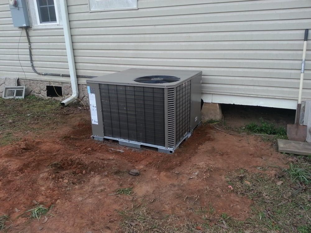 Outdoor air conditioner unit beside a beige house wall on bare dirt ground