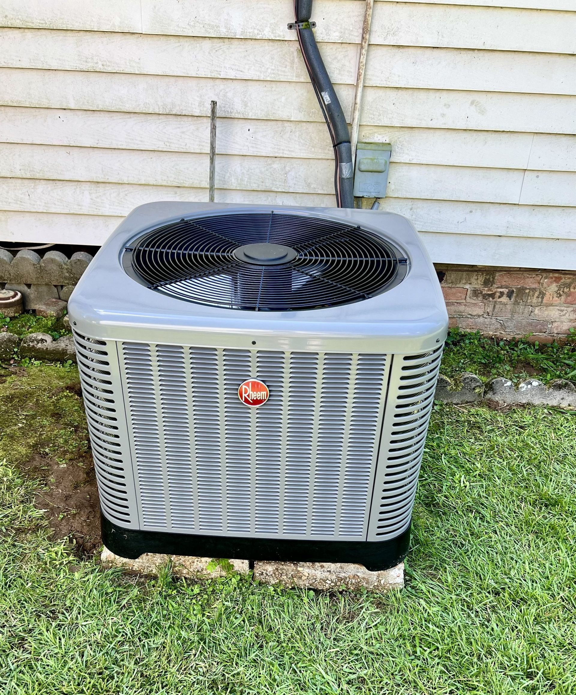 Outdoor air conditioner unit beside a house, with a fan on top and beige siding behind it
