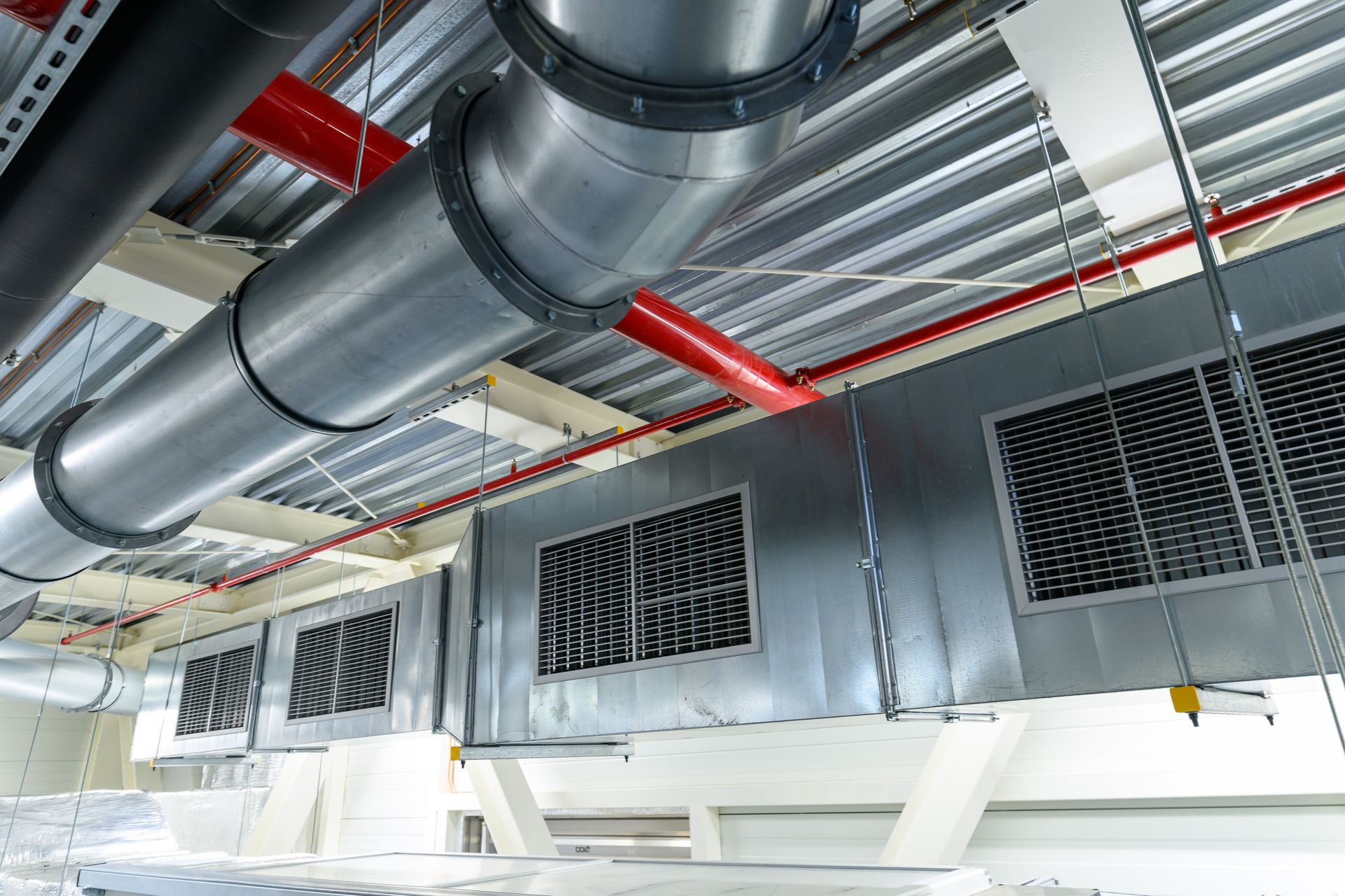 Large industrial HVAC ducts and vents on a ceiling in a mechanical room, with red pipe supports.
