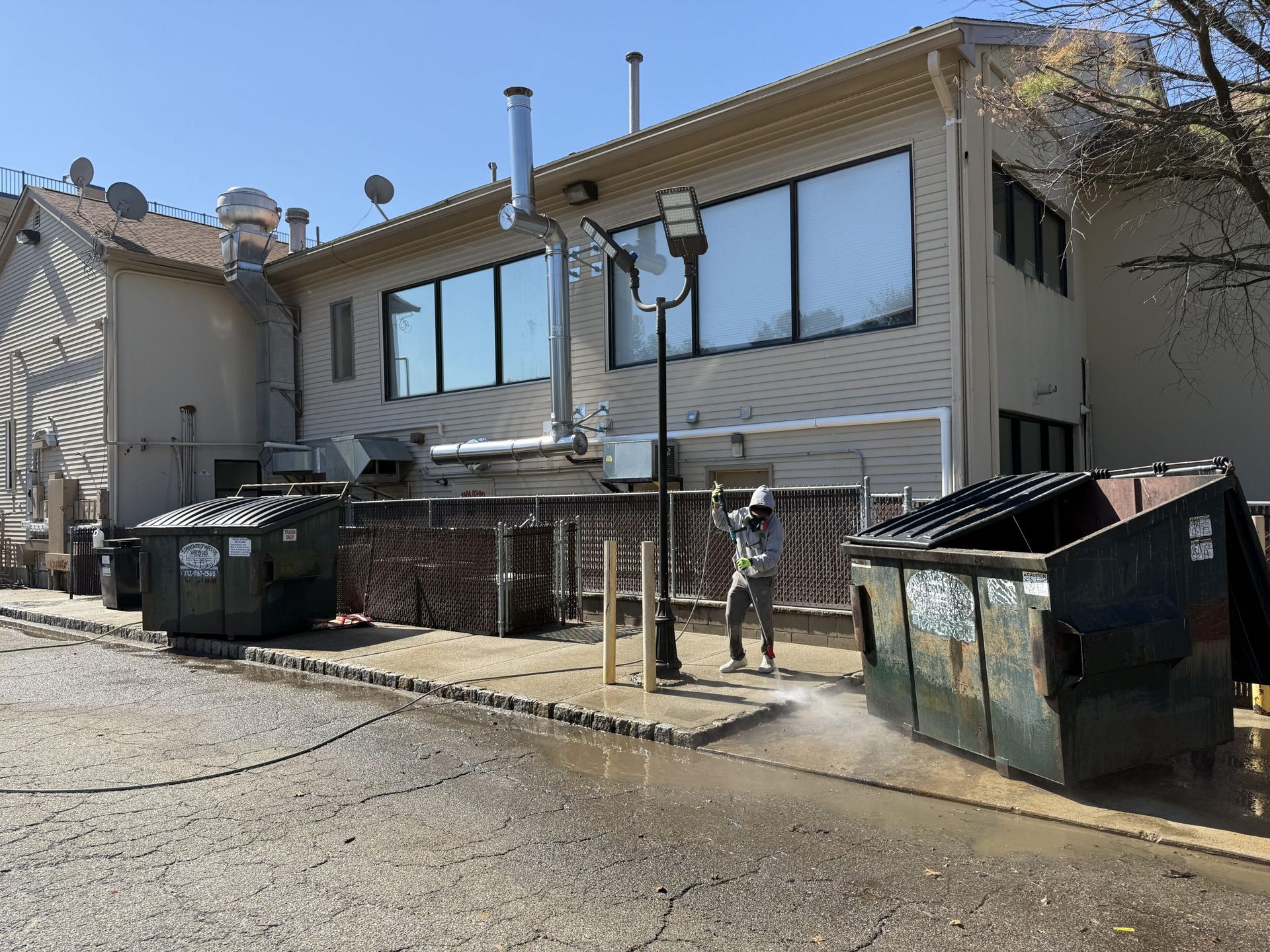 Street view of a house with large windows, garbage bins, and two people near the sidewalk