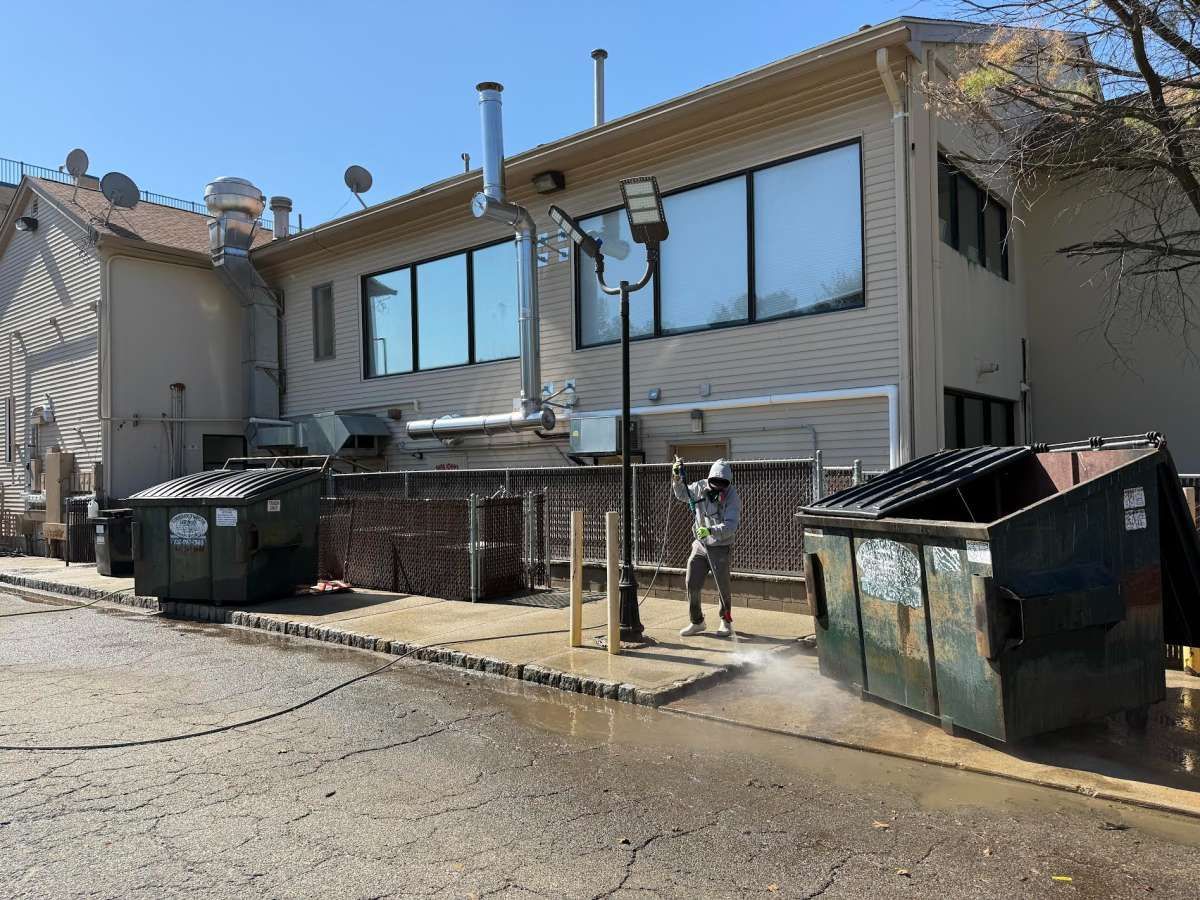 Two-story building with large windows and dumpsters on a sloped street, with a person standing outside.