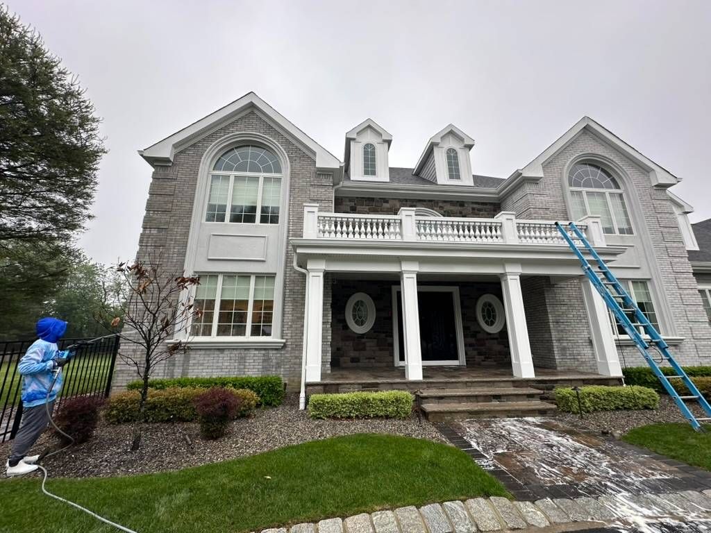 Two-story gray house with white trim; a person on a ladder trims near the roof and porch.