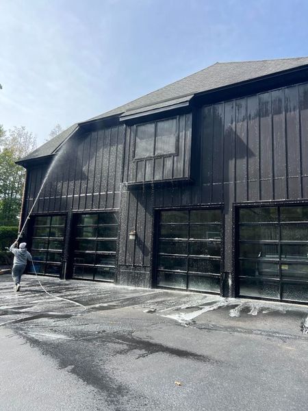 Charred black barn exterior with a person spraying water along the side in bright daylight