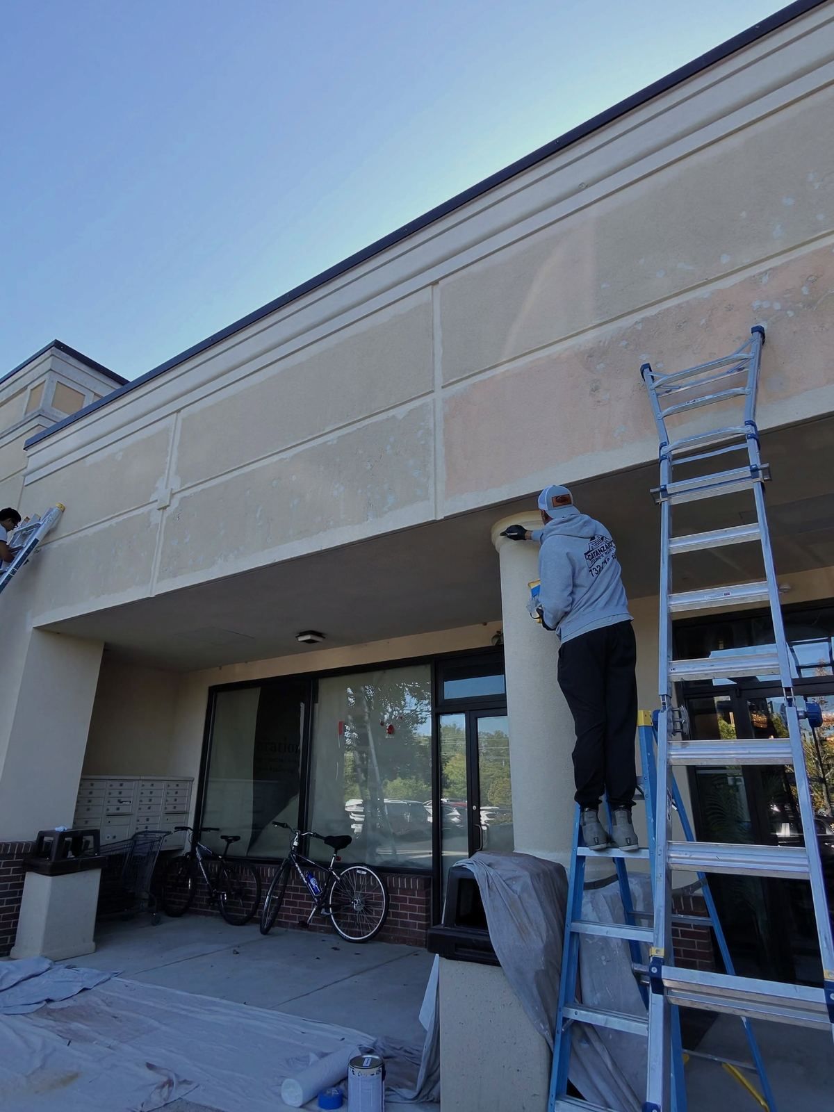 Crew on ladder washing strip mall facade — Catanzaro's Power Washing
