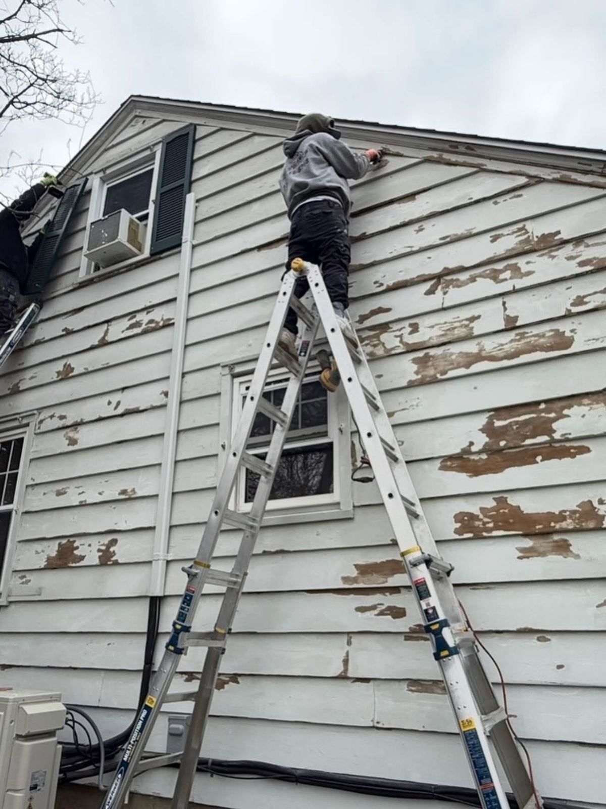 Painter on ladder scraping peeling siding — Catanzaro's Power Washing