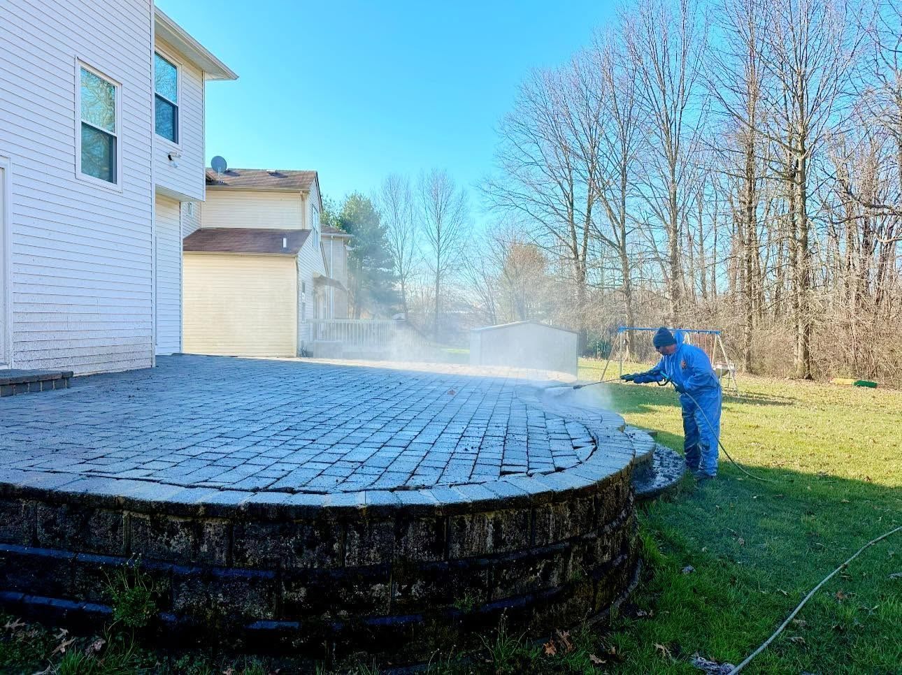 Round paver patio, worker power washing — Catanzaro's Power Washing