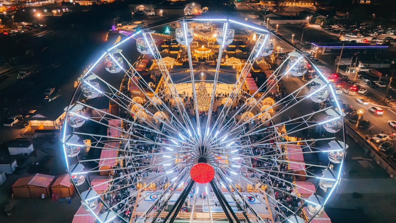 Ferris wheel glowing at night in a busy fairground, seen from above the Cullman Christkindlmarkt.