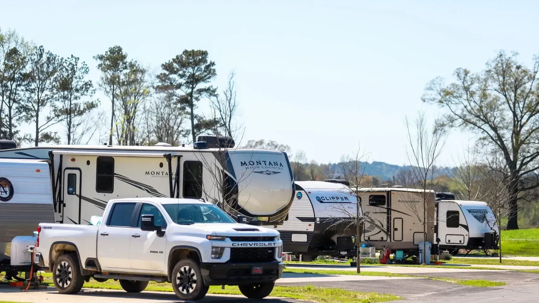 A row of rvs and trucks are parked in a campground.