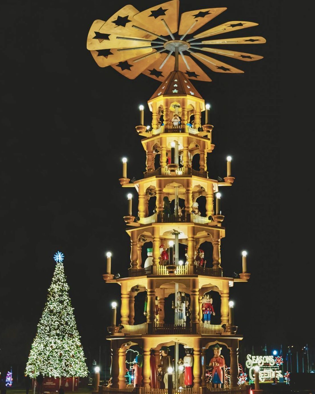A christmas tree and a pyramid are lit up at night