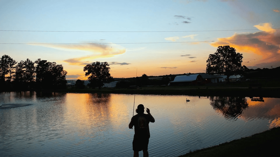 A man is fishing in a lake at sunset.