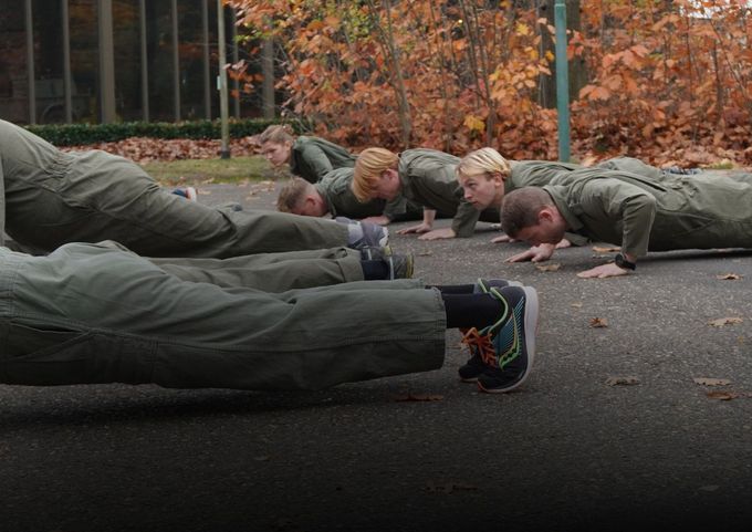 Mensen doen push-ups op een geplaveid pad in een park met herfstbomen.