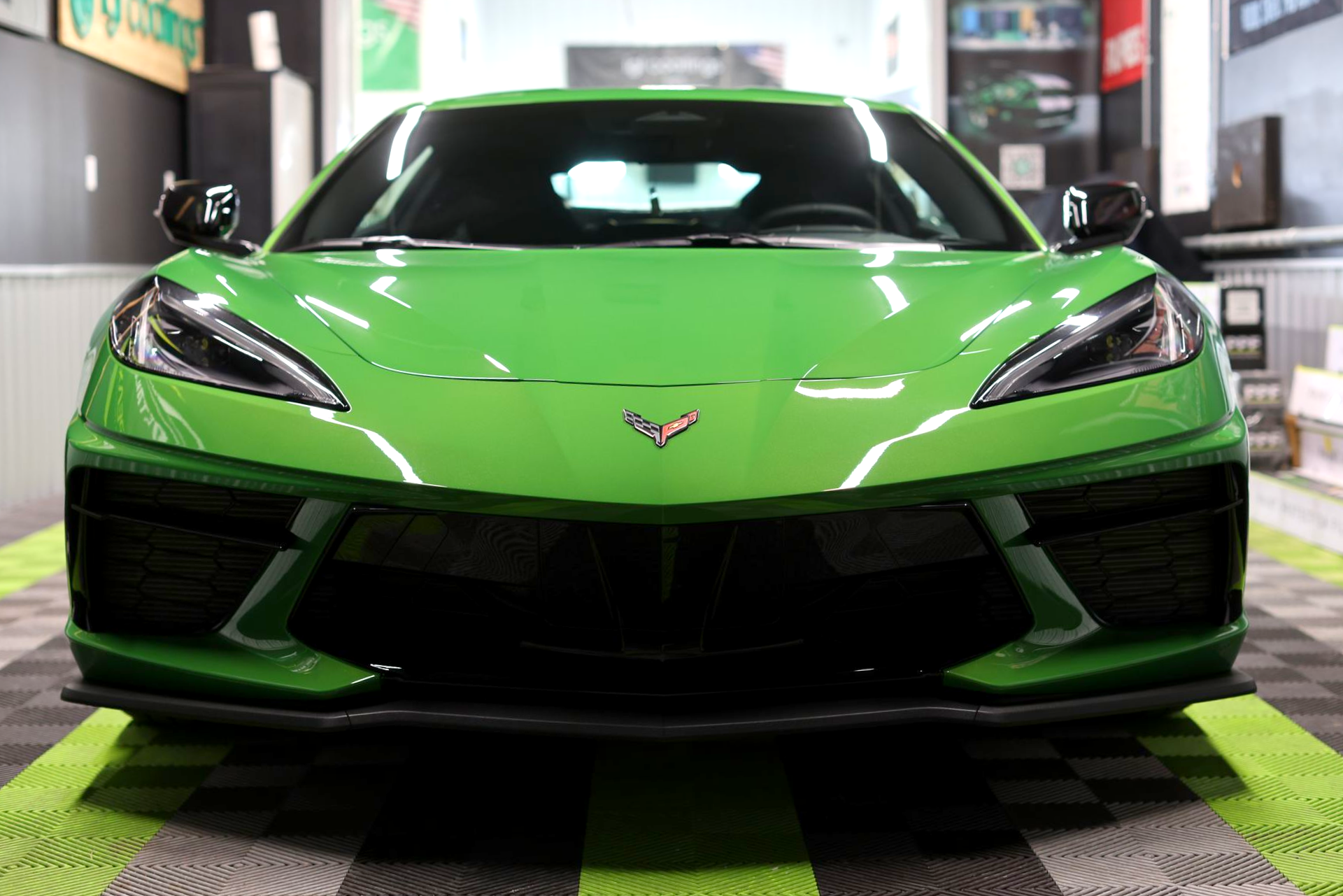 Green Chevrolet Corvette sports car in a garage, front view on a checkered floor.
