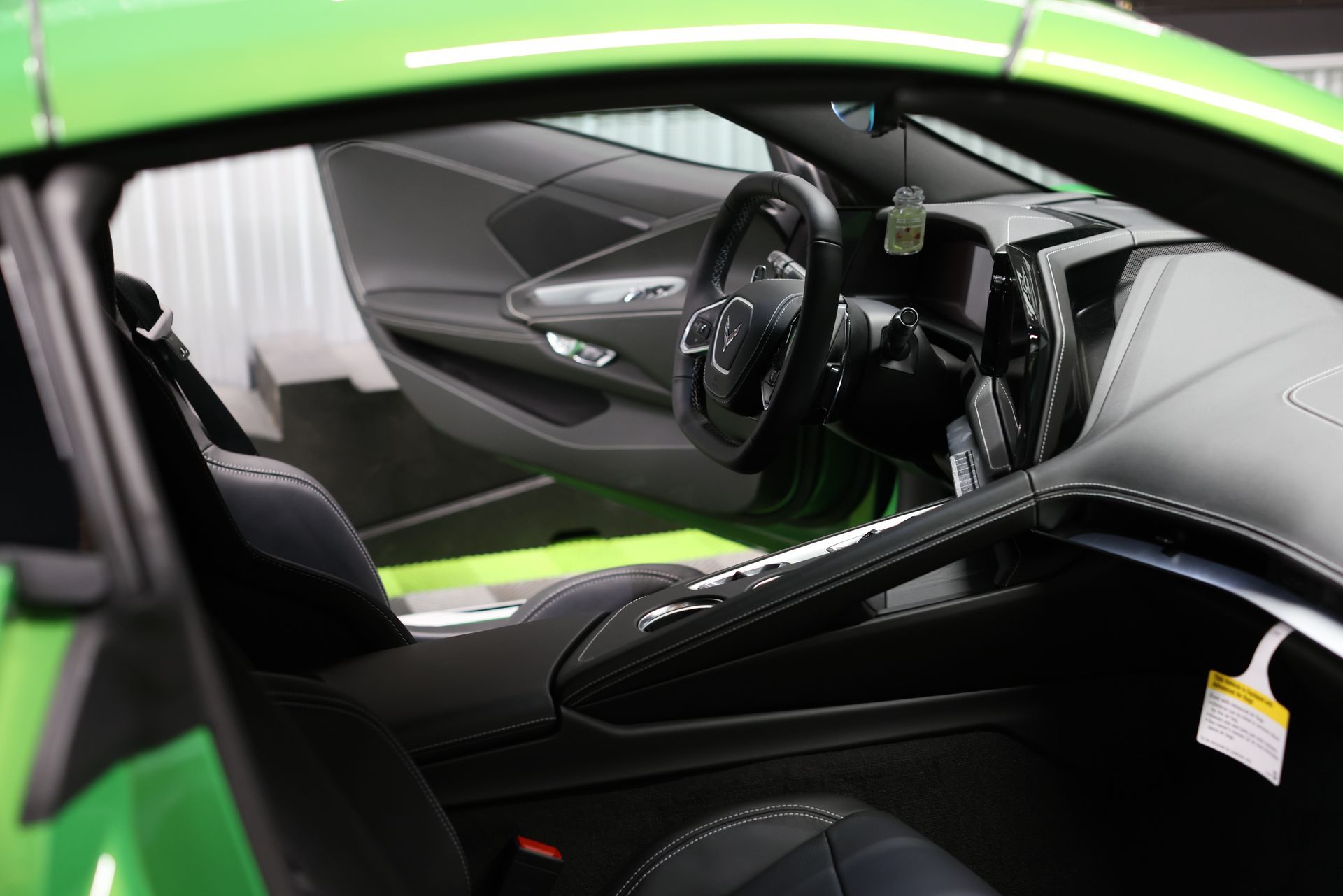 Green sports car interior with black seats and dashboard, viewed through the open driver-side door