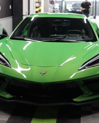 Front view of a bright green Corvette sports car indoors under showroom lights
