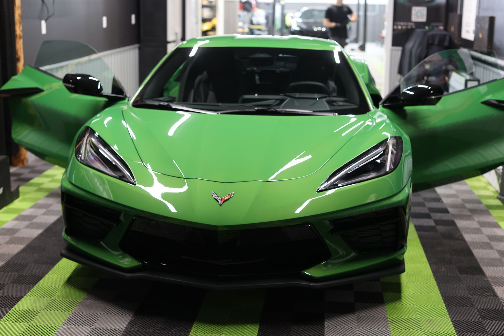 Green sports car with scissor doors open in a showroom, front view