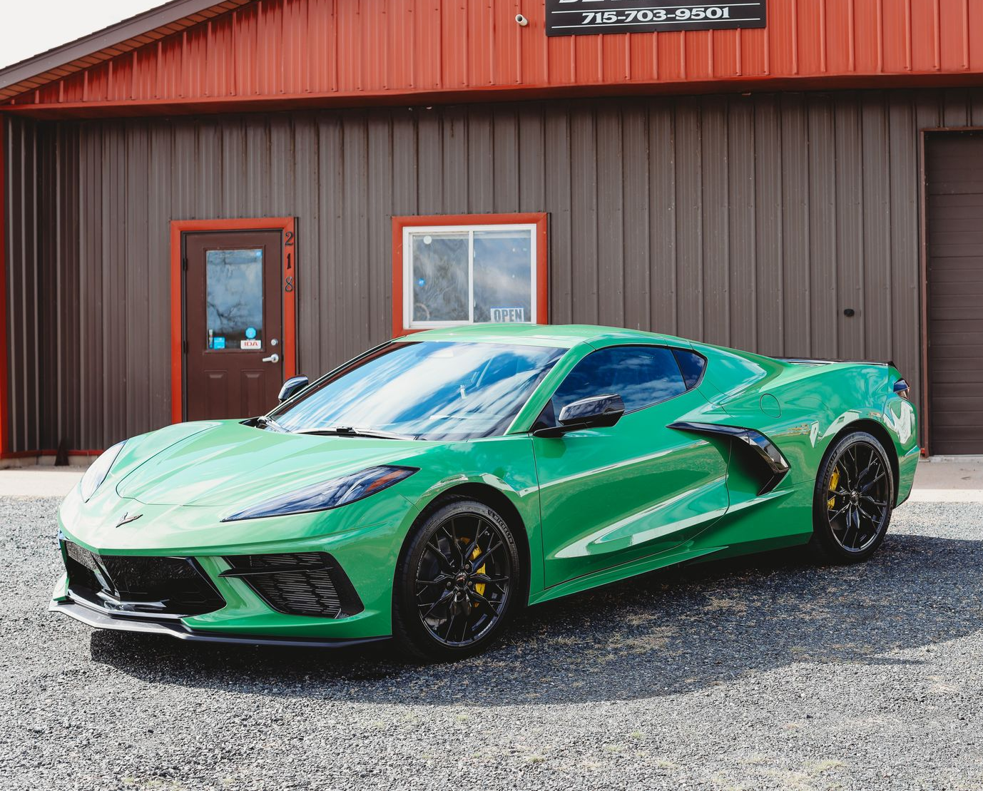 Bright green sports car parked outside a brown garage with a red roof on a gravel lot