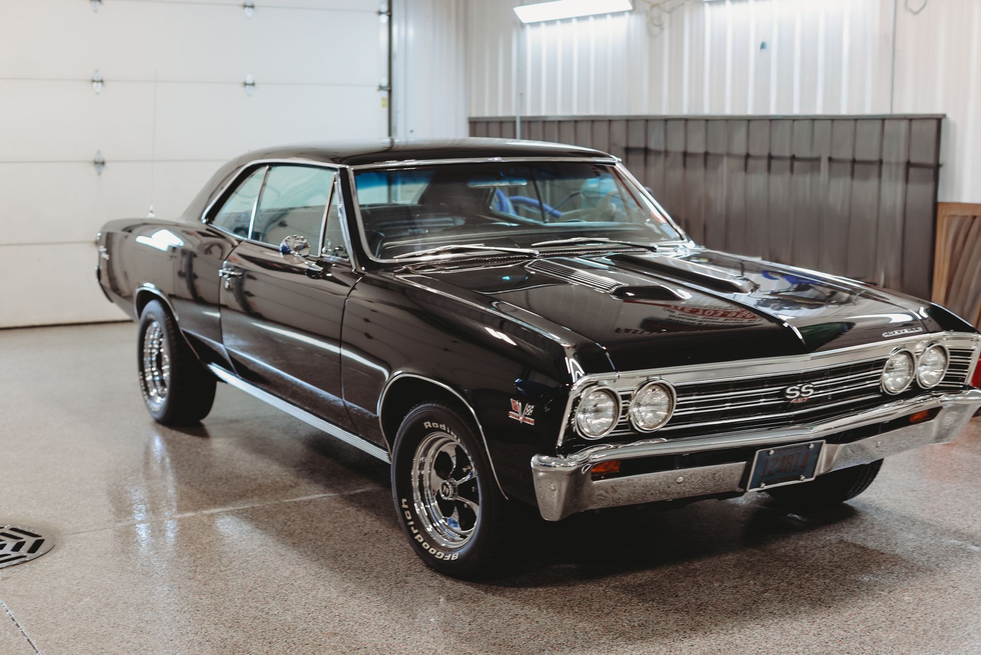 Classic black muscle car parked indoors in a bright garage, angled front-left view.