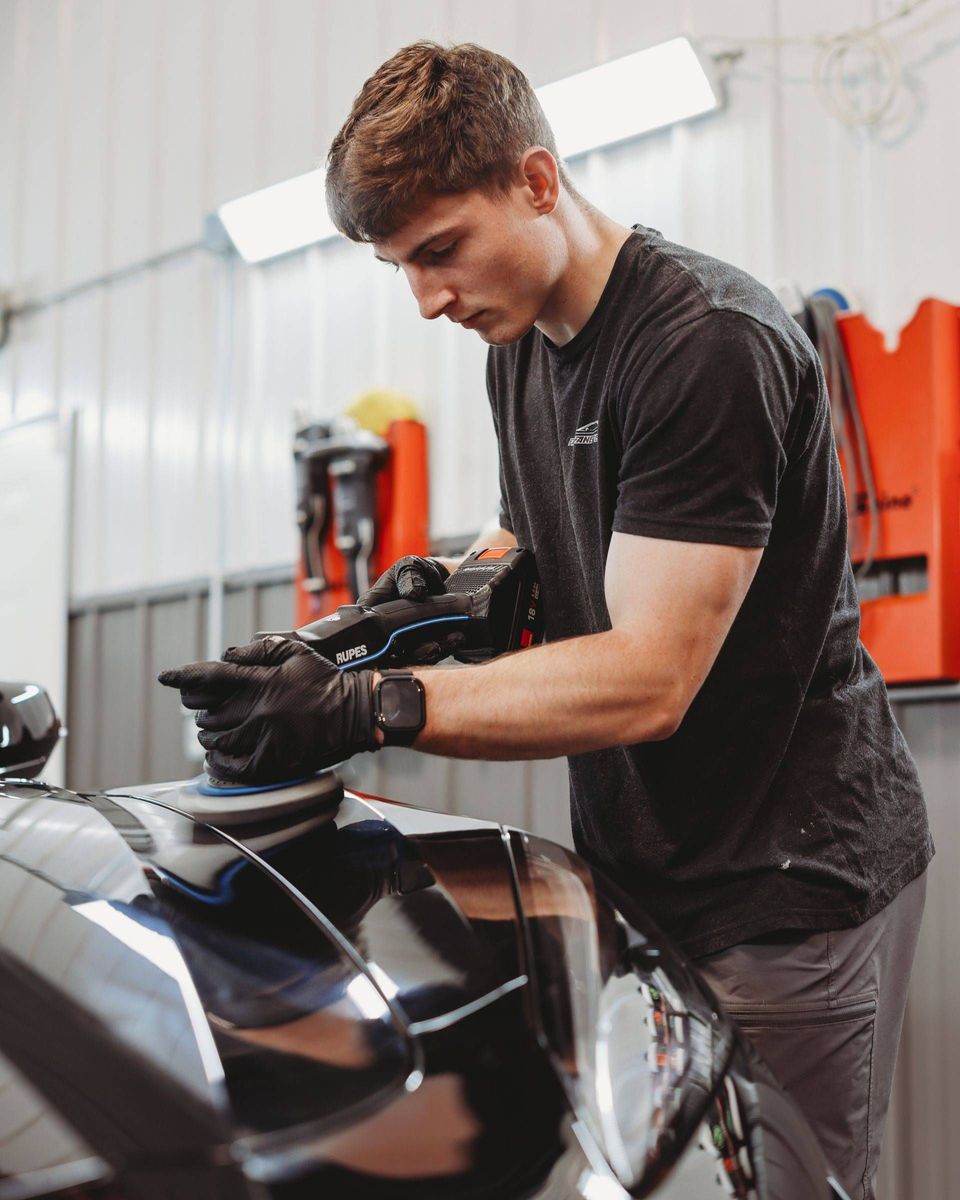 Mechanic polishing a black car in an auto shop, focused on detailing the hood