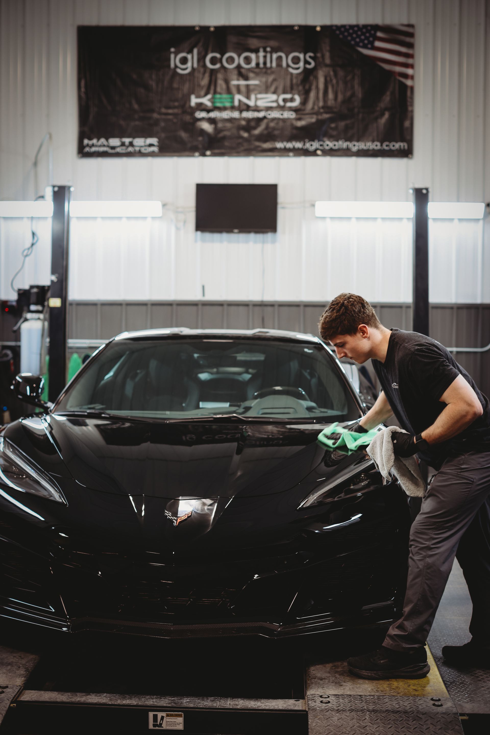 Man polishing a black sports car in a garage, with a banner overhead