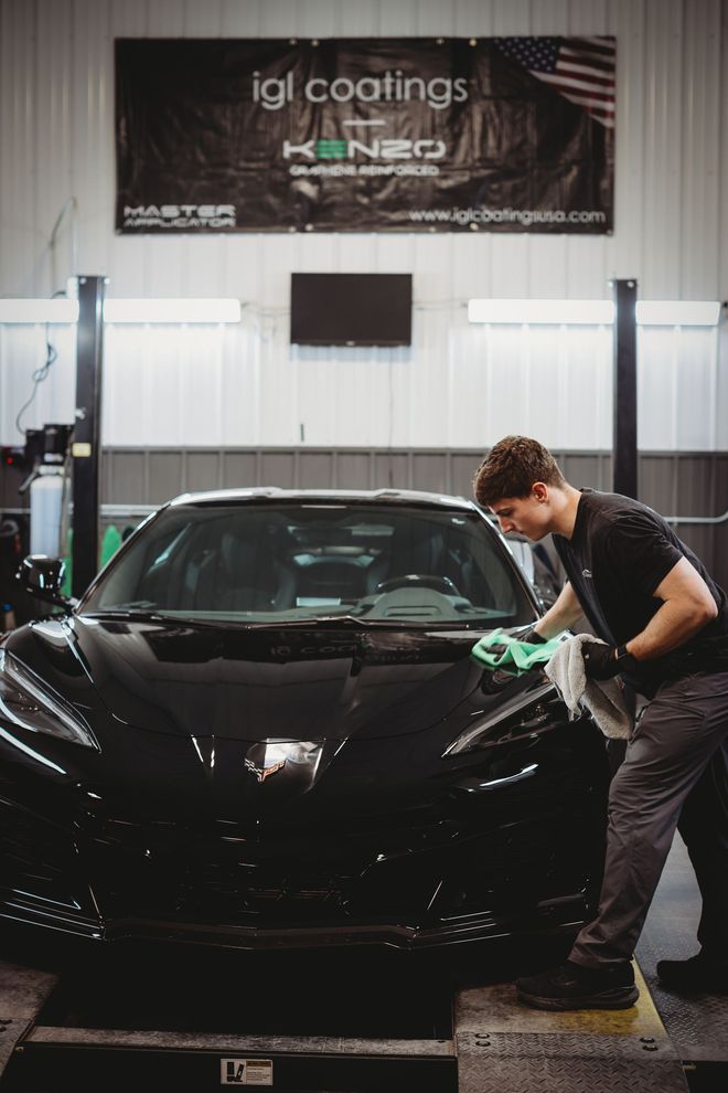 Detailing shop scene with a man polishing a black sports car under an IGI Coatings banner