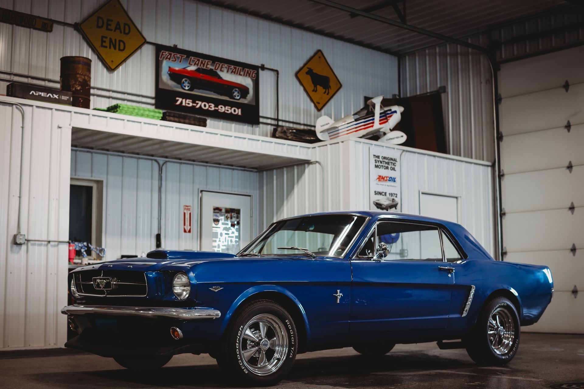 Blue classic muscle car in an auto shop garage, with service signs and equipment in the background