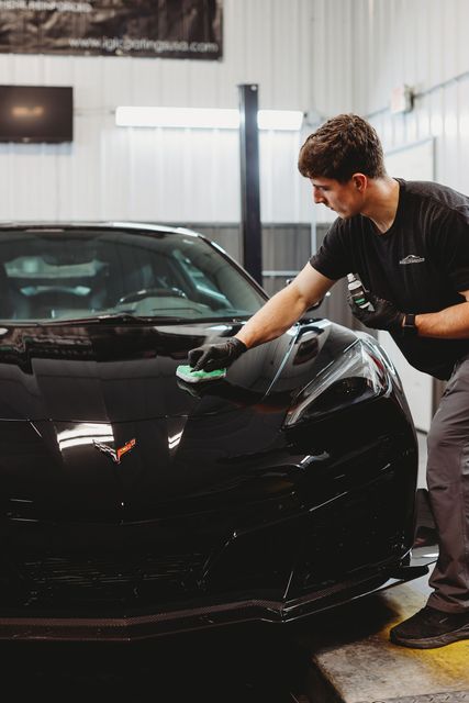 A person is polishing the hood of a blue car.