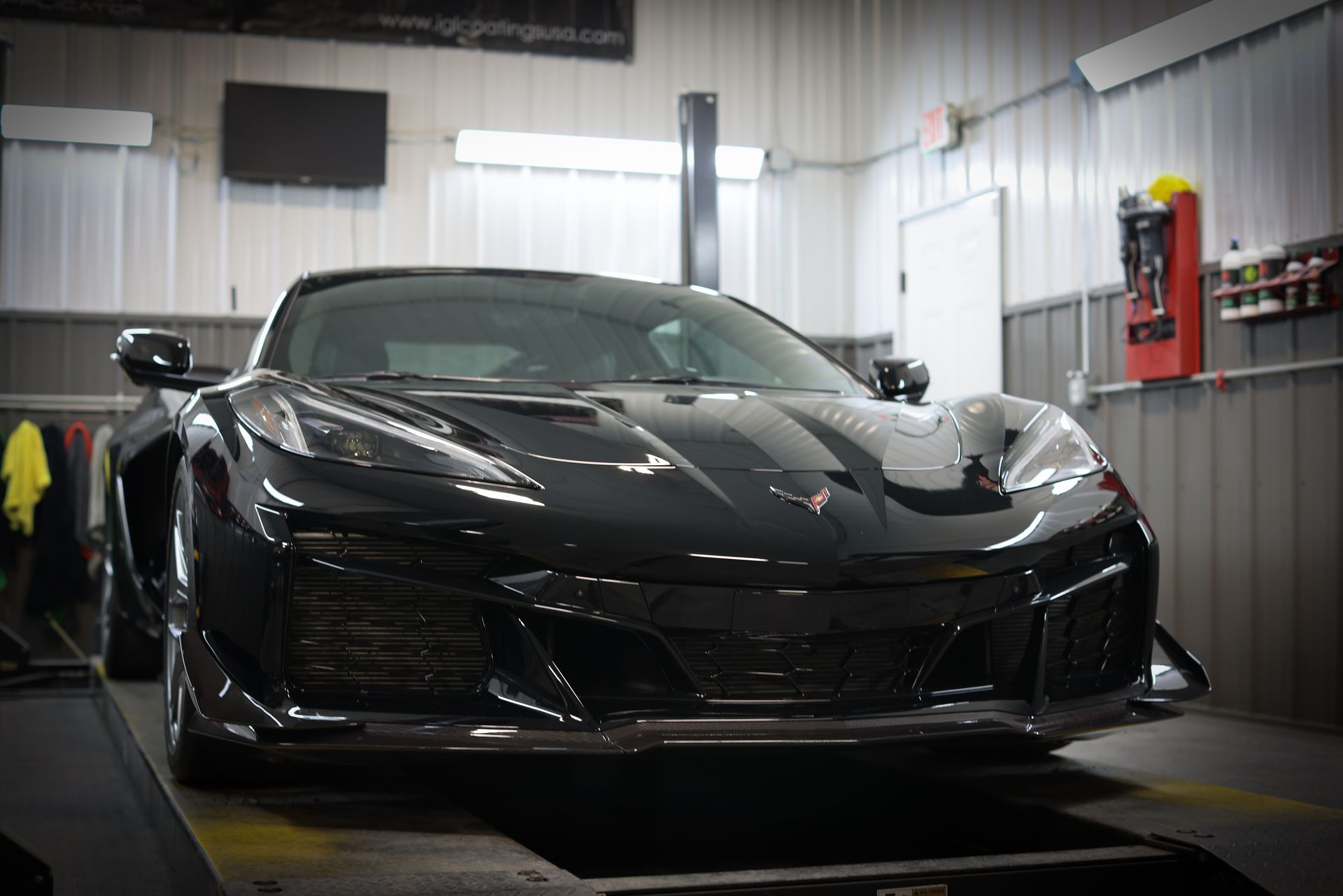 Black sports car in a garage or workshop, front view on a lift under bright lights