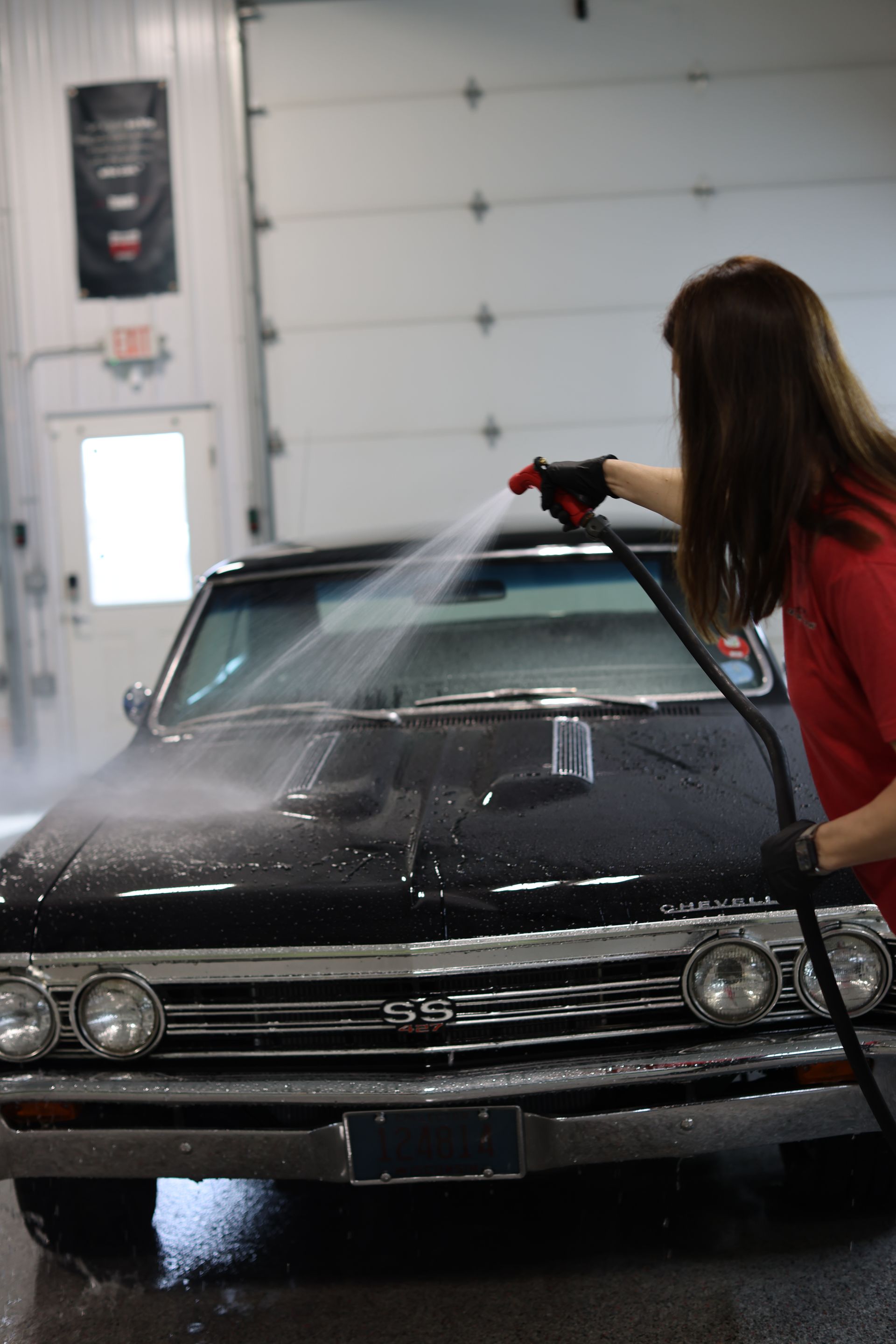 Person spraying water on a black classic car in a garage.