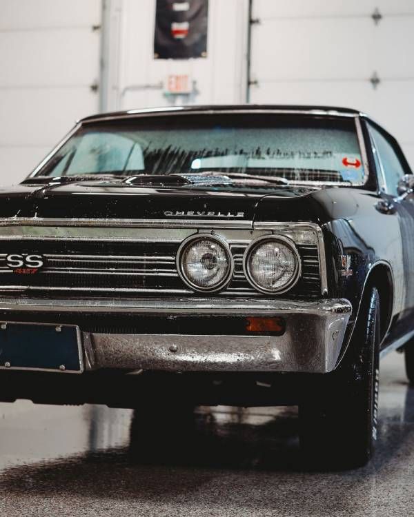 Front view of a black classic Chevrolet Chevelle SS in a garage, with chrome trim and twin round headlights