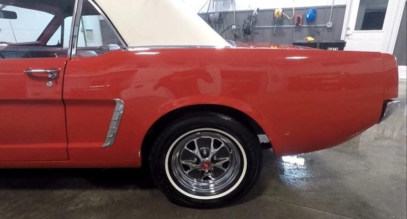 A red mustang with a white top is parked in a garage